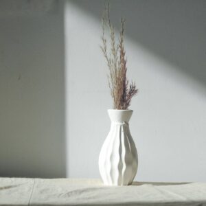 Minimalist white vase with decorative dried grass on a gray background, showcasing simplicity and elegance.